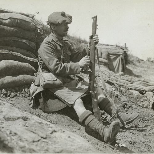 A soldier with a rifle sitting on the ground.