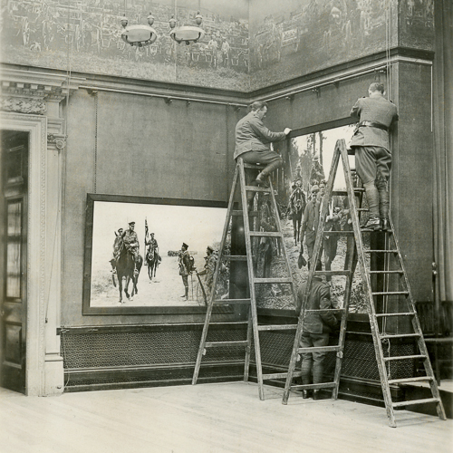 Two men on ladders hanging a painting.