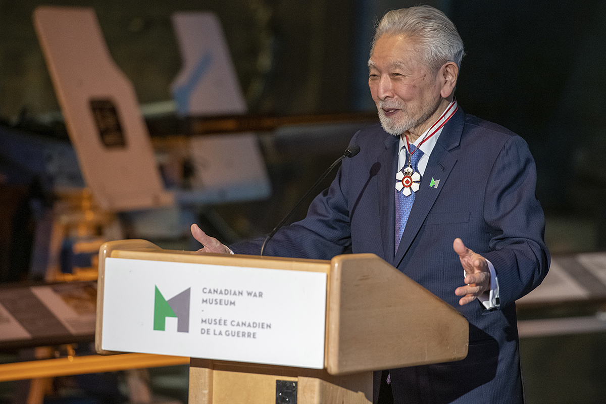 A man in a suit standing at a podium in the Canadian War Museum, Ottawa.