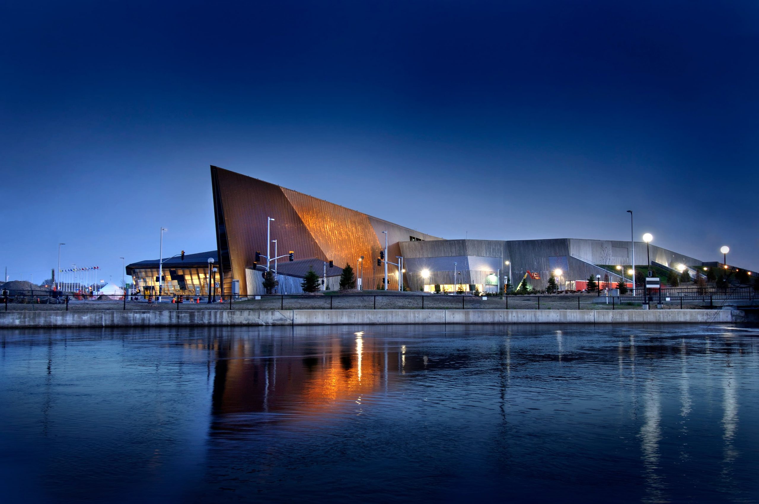 The Canadian War Museum in Ottawa is magnificently illuminated at night by a nearby body of water.