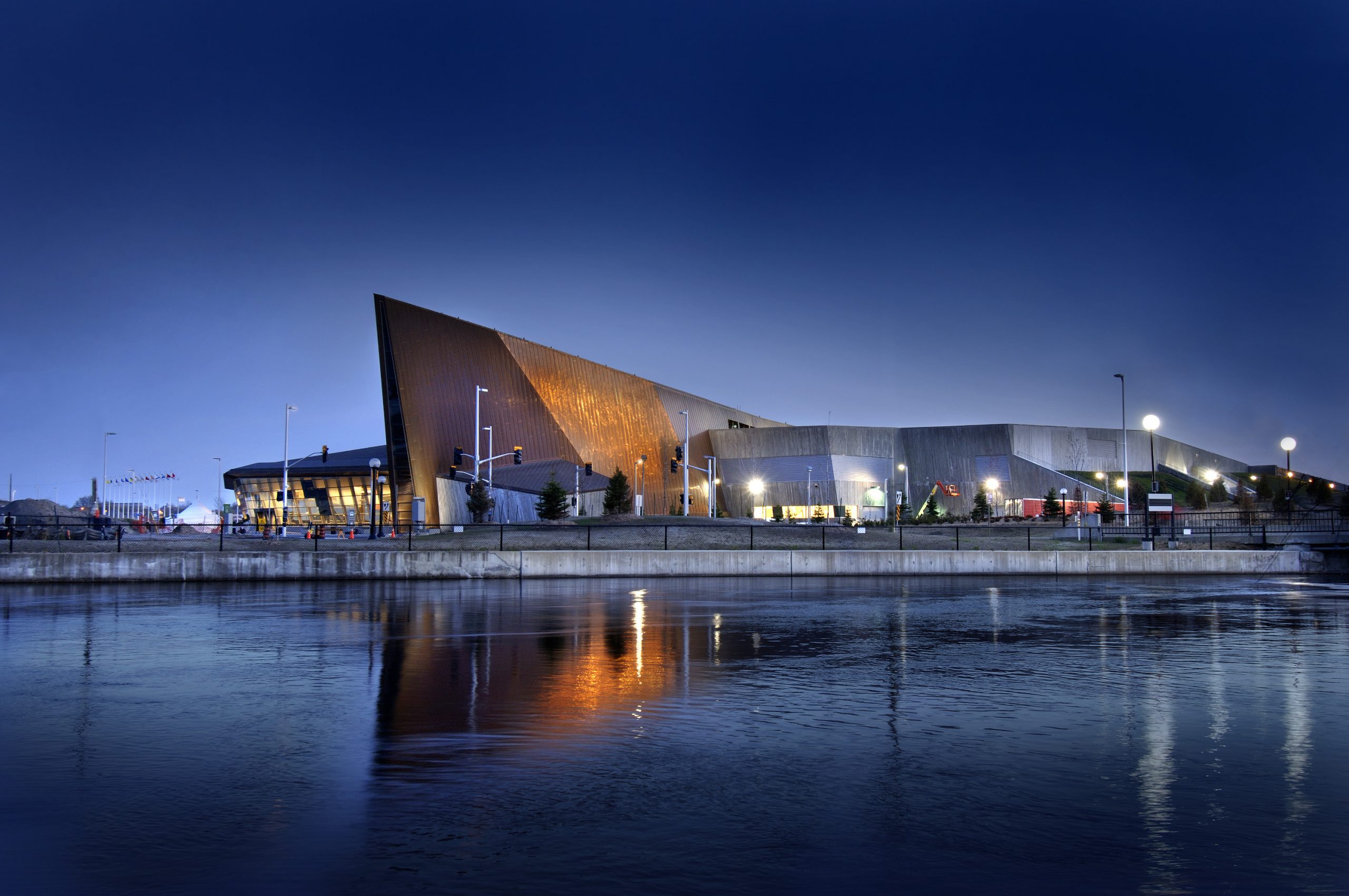 The Canadian War Museum stands illuminated at night, showcasing its stunning architecture and overlooking the peaceful body of water in Ottawa.