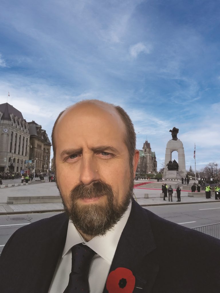 A man in a suit and tie standing in front of the Tomb of the Unknown Soldier in Ottawa.