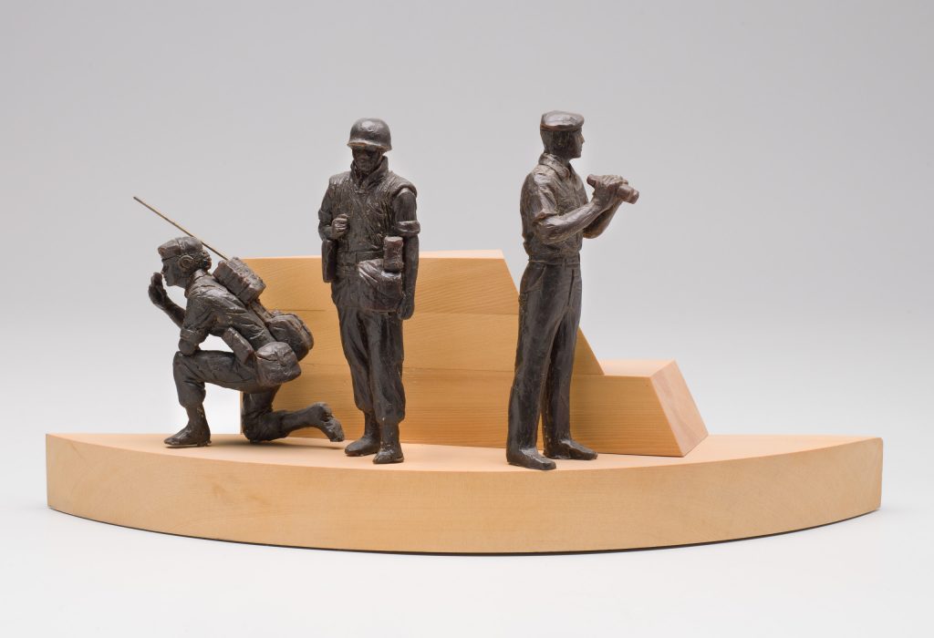 A bronze sculpture of three peacekeepers on a wooden base.