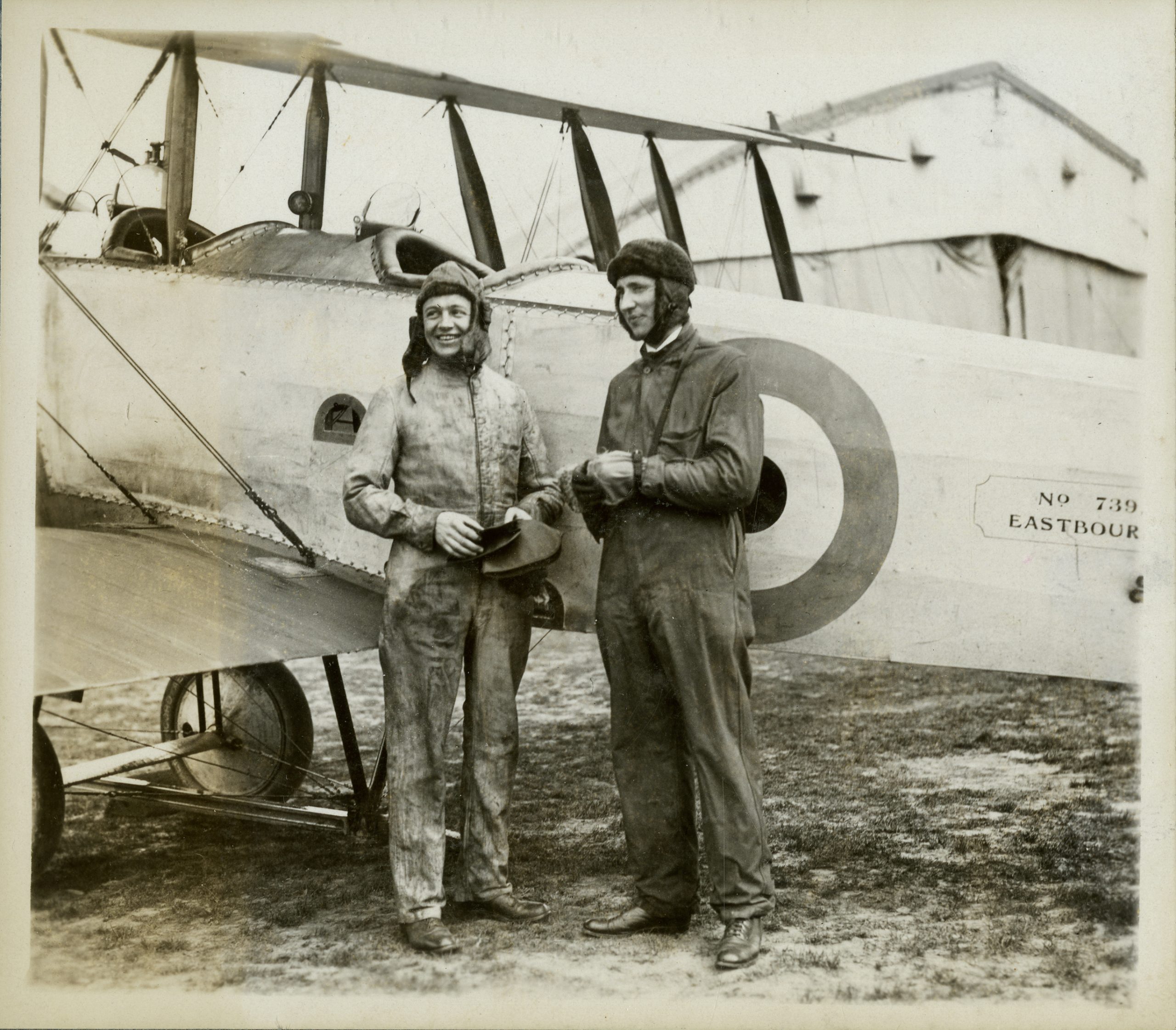 Two pilots standing in front of a WWI plane.